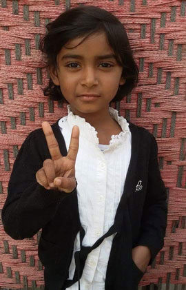 A school girl with a hand in her pocket making the peace sign