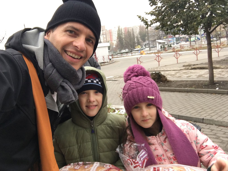 one man and two children dressed in hats and scarfs smiling on a foggy day