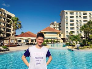 Man wearing a shirt with the words hunger inspired me to give in front of a swimming pool in a hot place