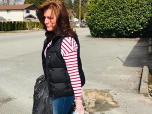 Woman in vest and striped shirt carrying a garbage bag and wearing gloves