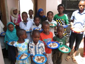 Orphans of Arusha, Tanzania holding plates of beans and rice indoors