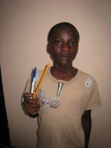 Abdalah holding writing utensils with a shirt that reads the art of progress