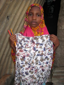 orphan of arusha holding a patterned cloth and writing utensils